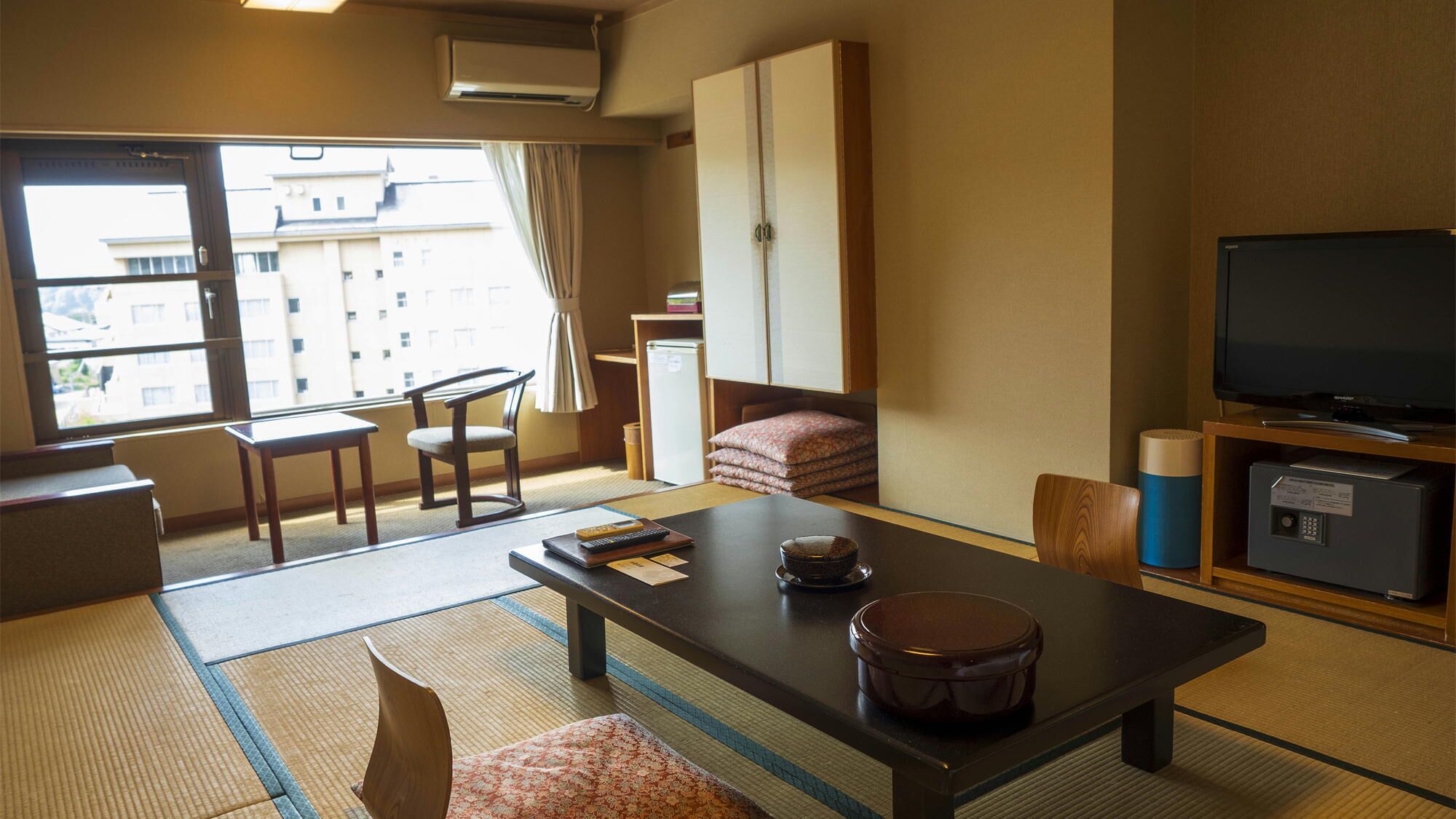 A hotel room with tatami flooring, a low table with a bowl and chopsticks, a sofa, a television, and a cabinet with a remote control.