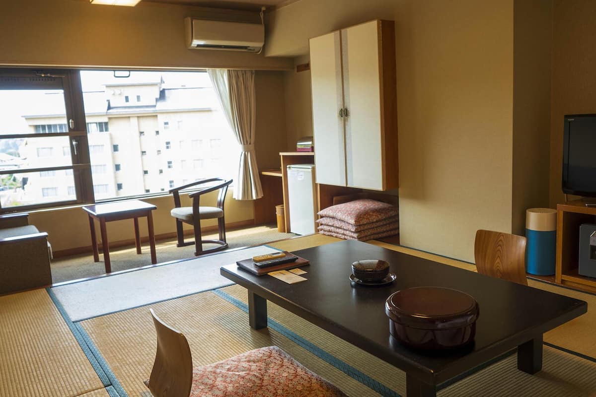 Une chambre d’hôtel avec un sol recouvert de tatamis, une petite table avec un bol et des baguettes, un canapé, une télévision et un meuble contenant une télécommande.