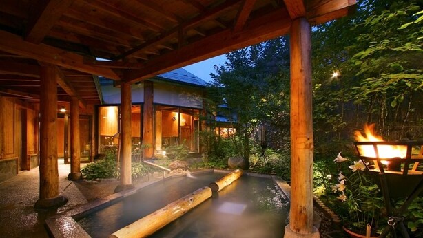 A traditional Japanese onsen with wooden beams and a stone bath. - Aishinkan (Morioka)