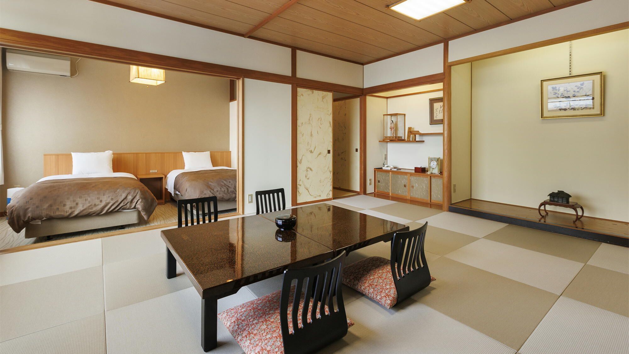 A traditional Japanese-style room with tatami flooring, a low table with chairs, and a bed with a wooden headboard.