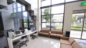 A modern waiting area with a computer desk, a couch, and large windows offering a view of the outdoors. - Mihara City Hotel (Mihara)