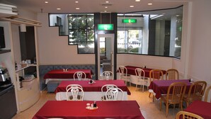 A restaurant with multiple tables and chairs, a counter with a display, and a large window with a view of the outside. - Mihara City Hotel (Mihara)