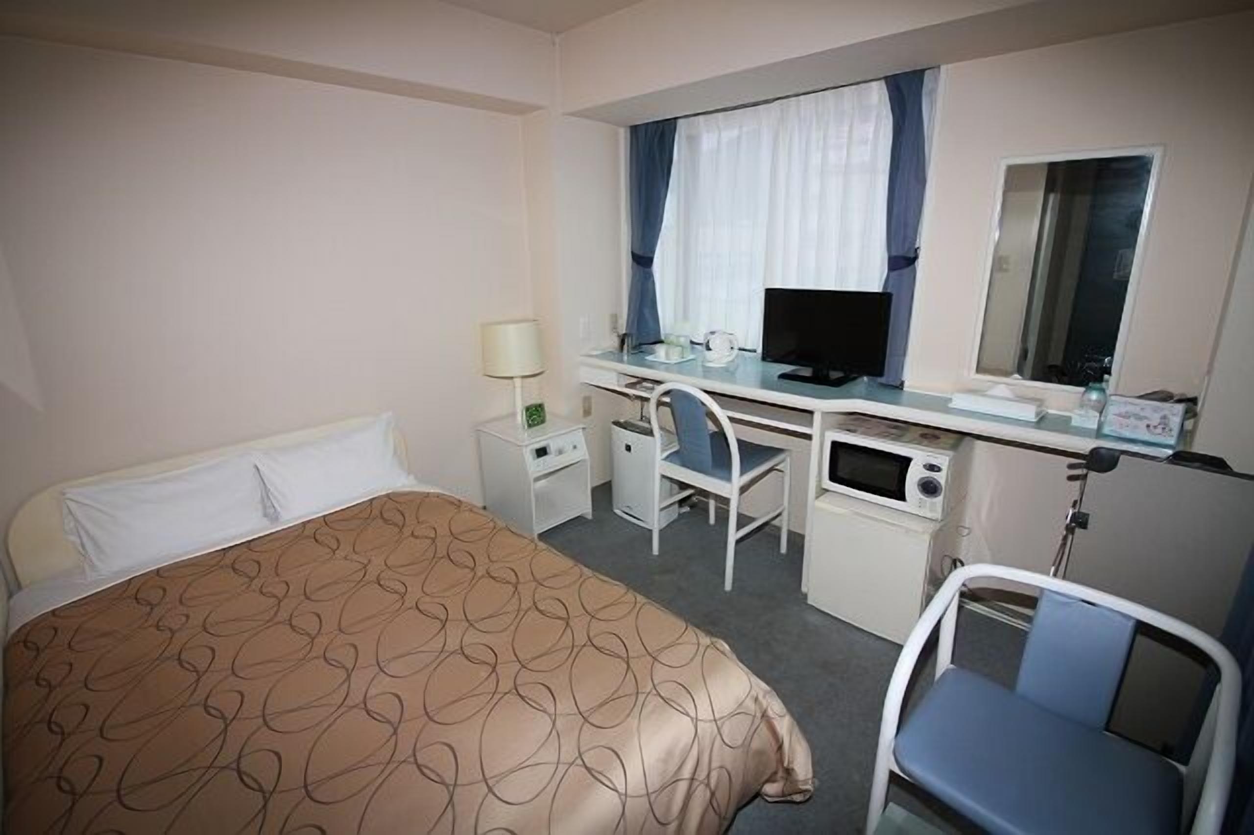Ein Hotelzimmer mit Bett, Schreibtisch, Stuhl, Fernseher und Spiegel.