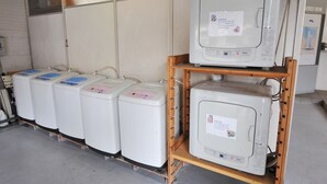 A row of white refrigerators and a microwave on a wooden shelf in a room with tiled walls. - Mihara City Hotel (Mihara)