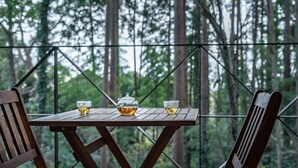 A wooden table with a teapot and two glasses, set against a forest backdrop. - Izukogen Onsen Hananokumo (Ito)