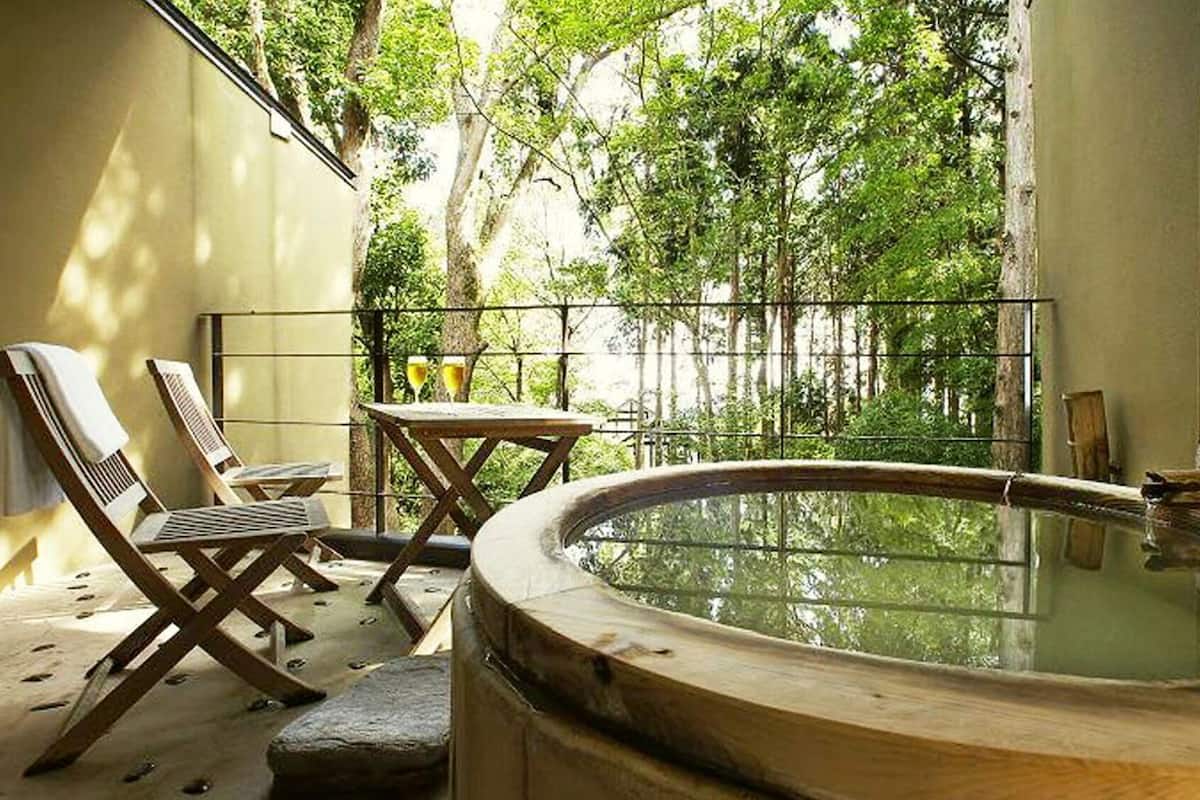 Ein Whirlpool mit Holzkante, zwei Liegestühle, ein kleiner Tisch mit Getränken und Blick auf einen bewaldeten Bereich.