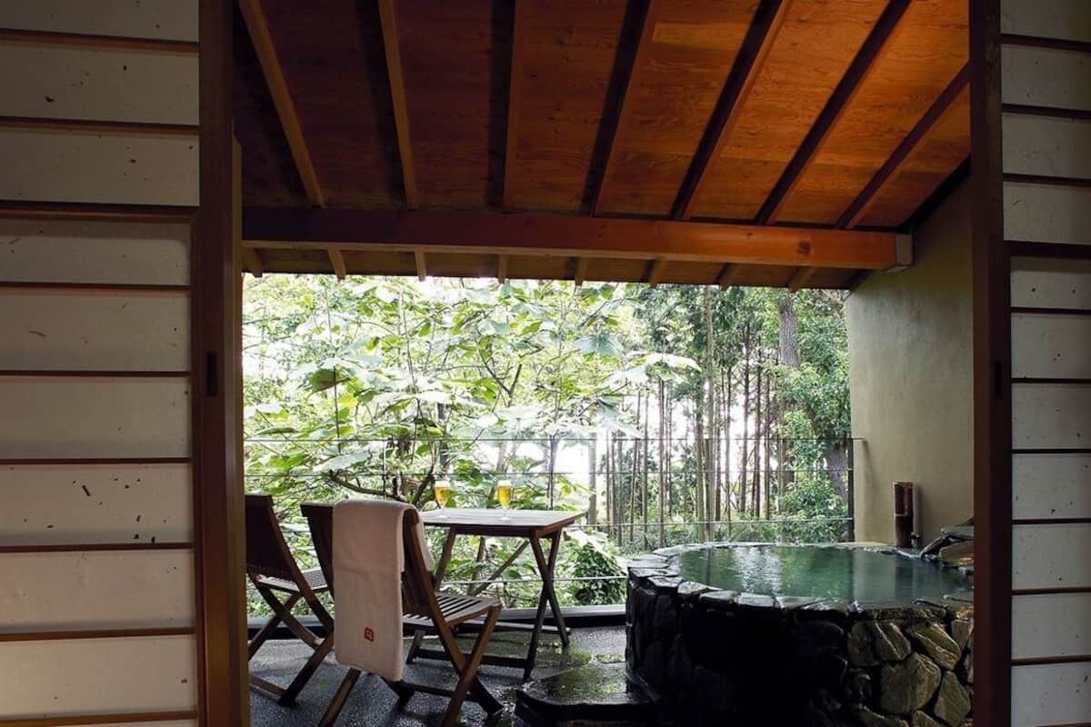 Ein überdachter Patio mit einem Steinhottub, Holzmöbeln und Blick auf einen üppigen Garten.