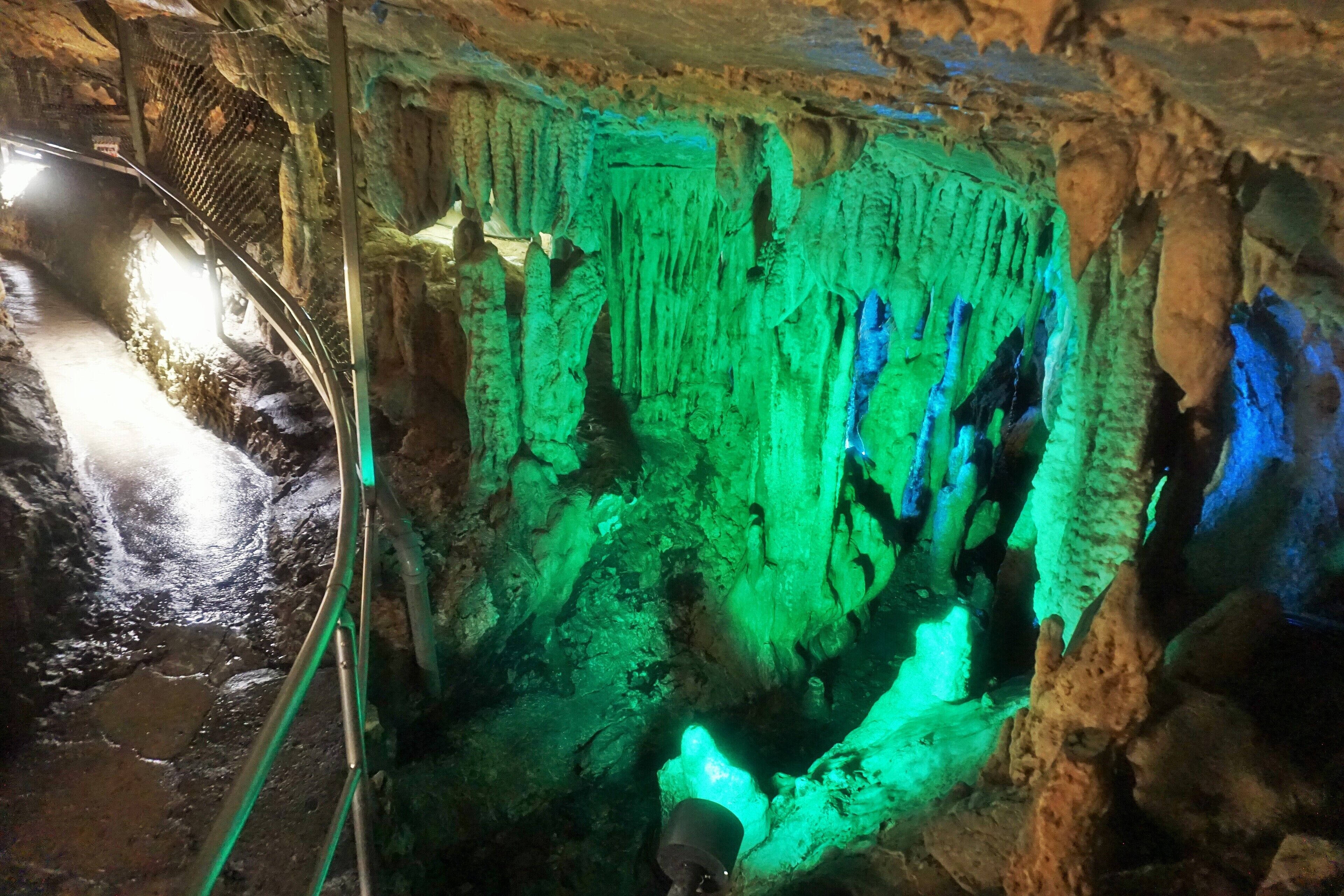A cave with green and blue illuminated stalactites.