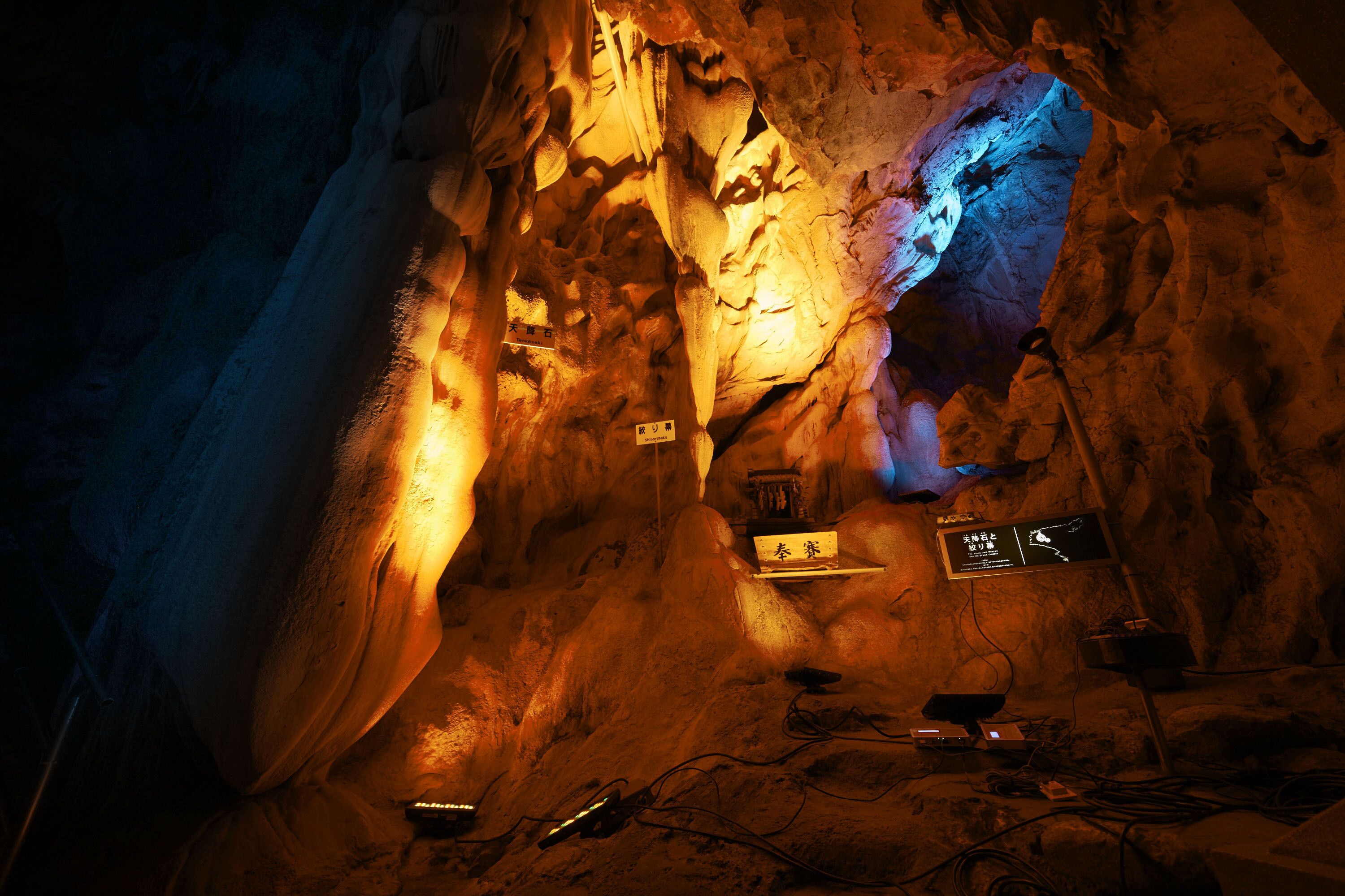 L’intérieur d’une grotte, orné de stalactites et éclairé par un système d’éclairage artificiel, ainsi que de panneaux d’information.