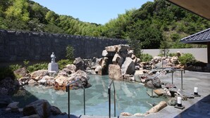 Una piscina cristalina con rocas y una estatua, rodeada por un muro de piedra y vegetación.