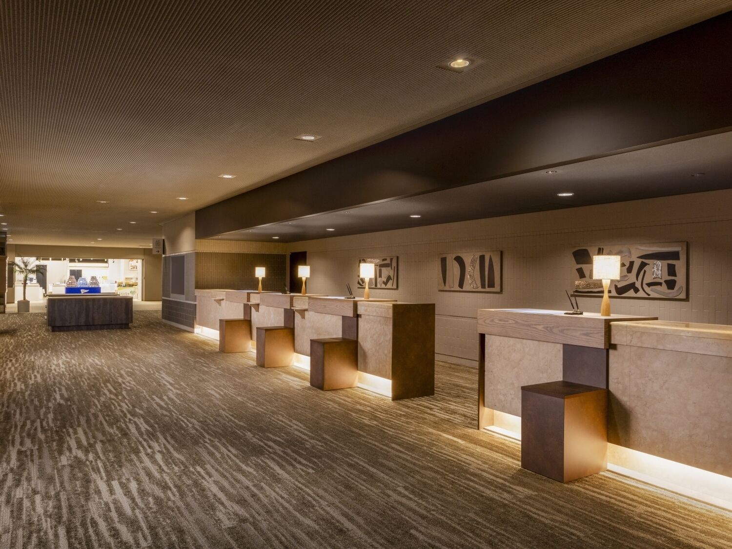 A hotel lobby with a reception desk, artwork on the walls, and a carpeted floor.