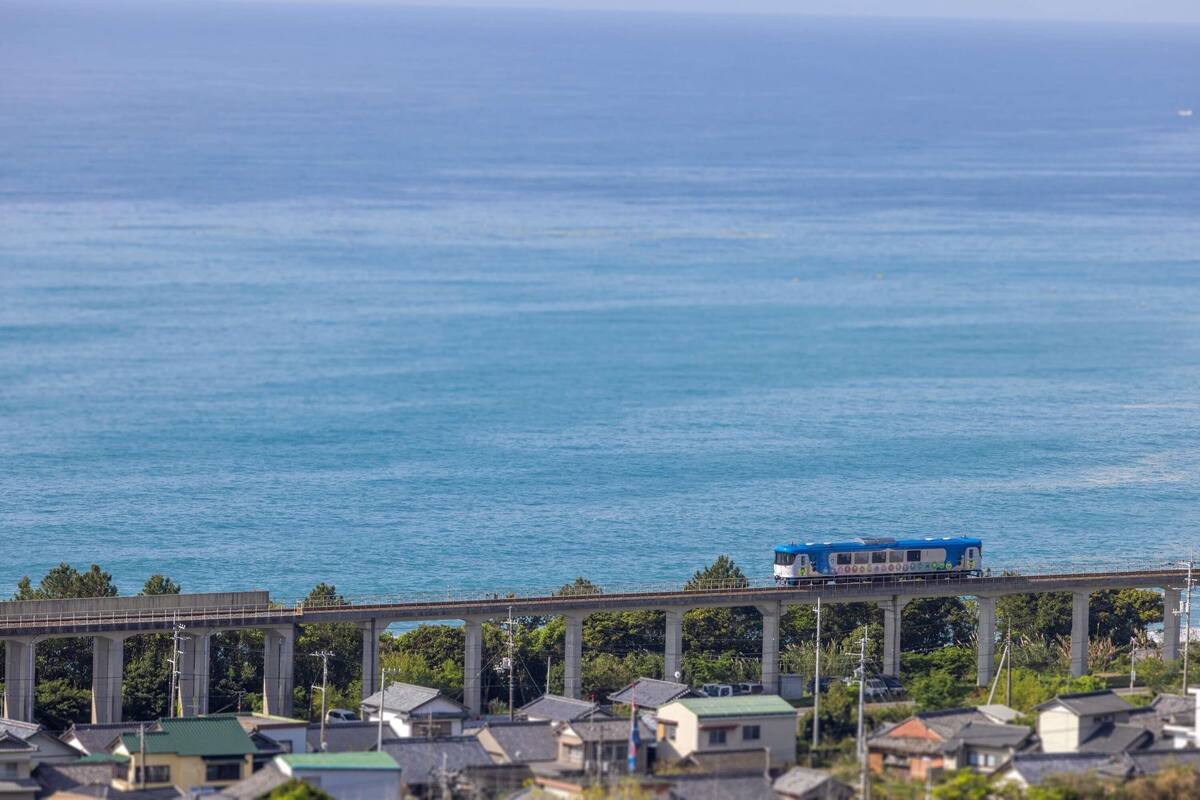 A blue train on a bridge over water.
