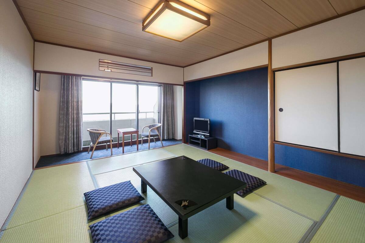 A traditional Japanese room with tatami flooring, a low table, a television, and a sliding door.