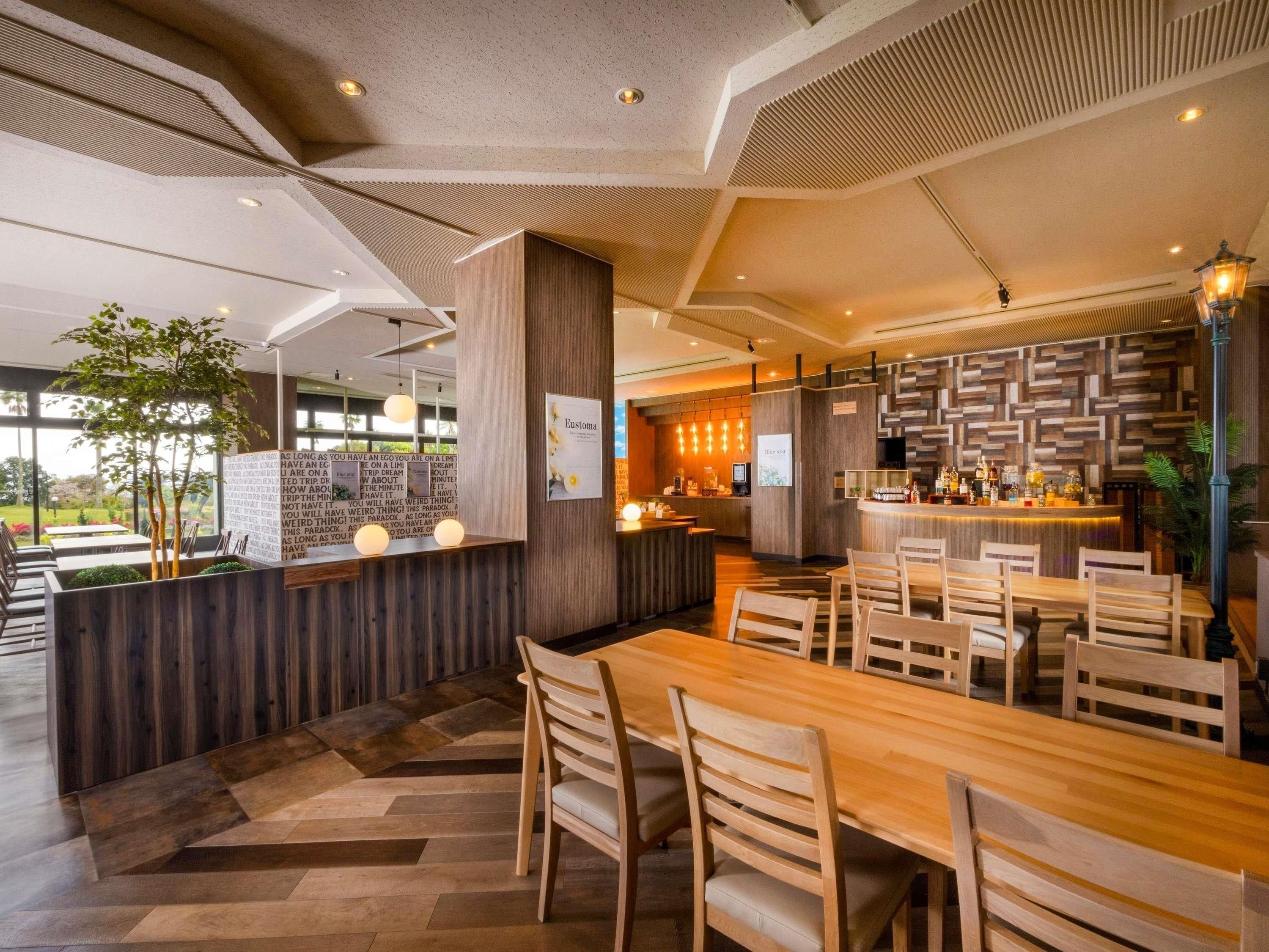 En modern restaurang med ett långt träbord och stolar, en bardisk och utsikt över omgivningarna.