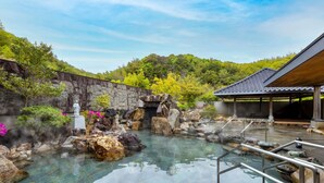 Un onsen japonés tradicional con una bañera de piedra, una estatua y un pabellón de madera.