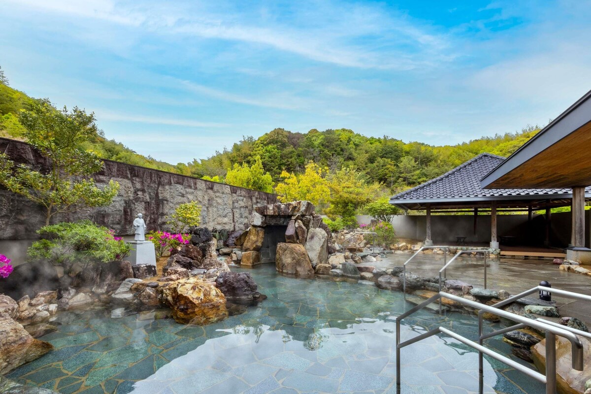 Un onsen japonais traditionnel, avec un bain en pierre, une statue et un pavillon en bois.