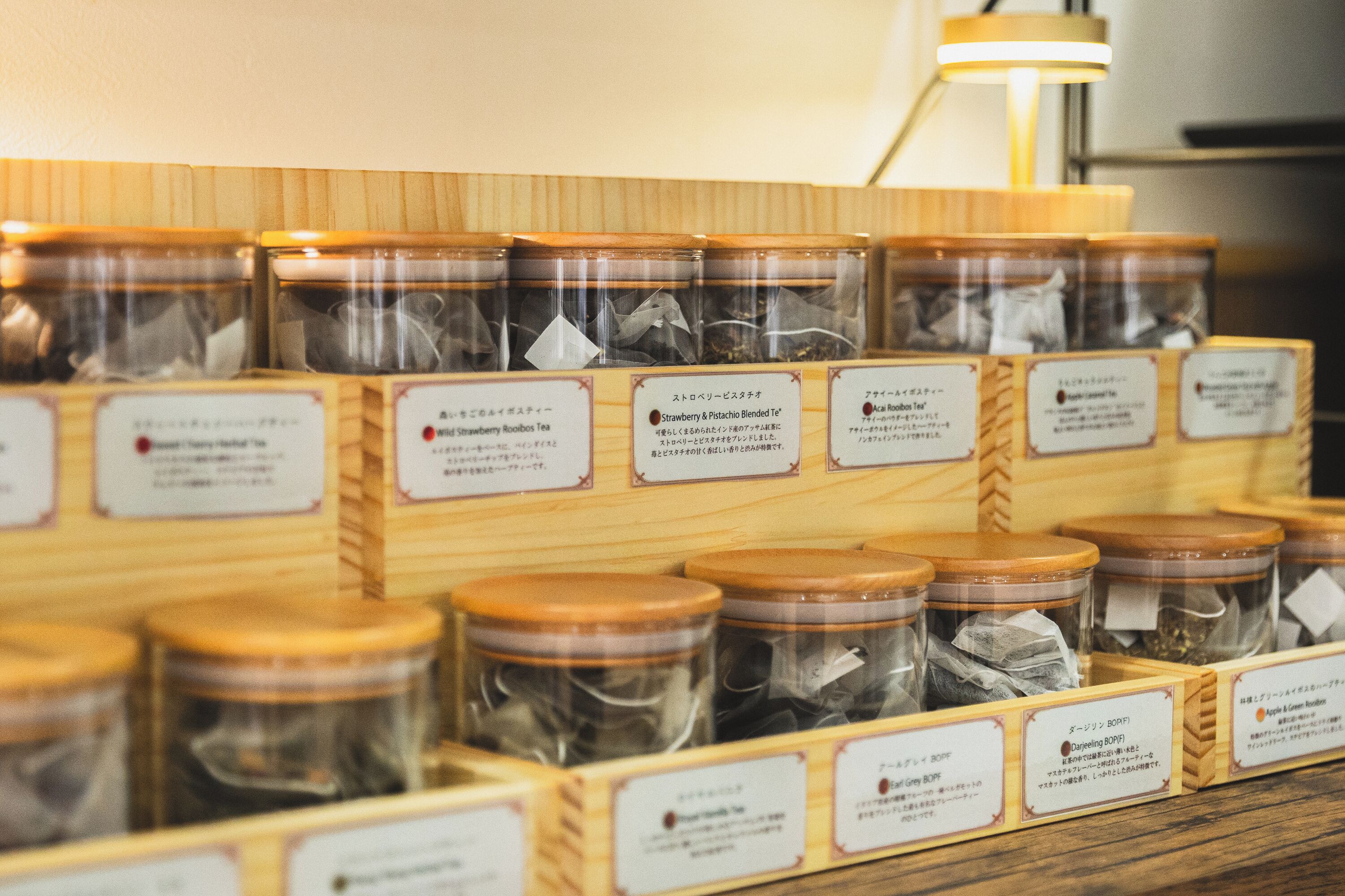 A display of tea varieties in glass jars with labels, arranged on wooden shelves.