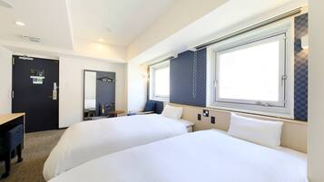 A hotel room with two beds, a desk, a chair, a small table, and a window with blinds.