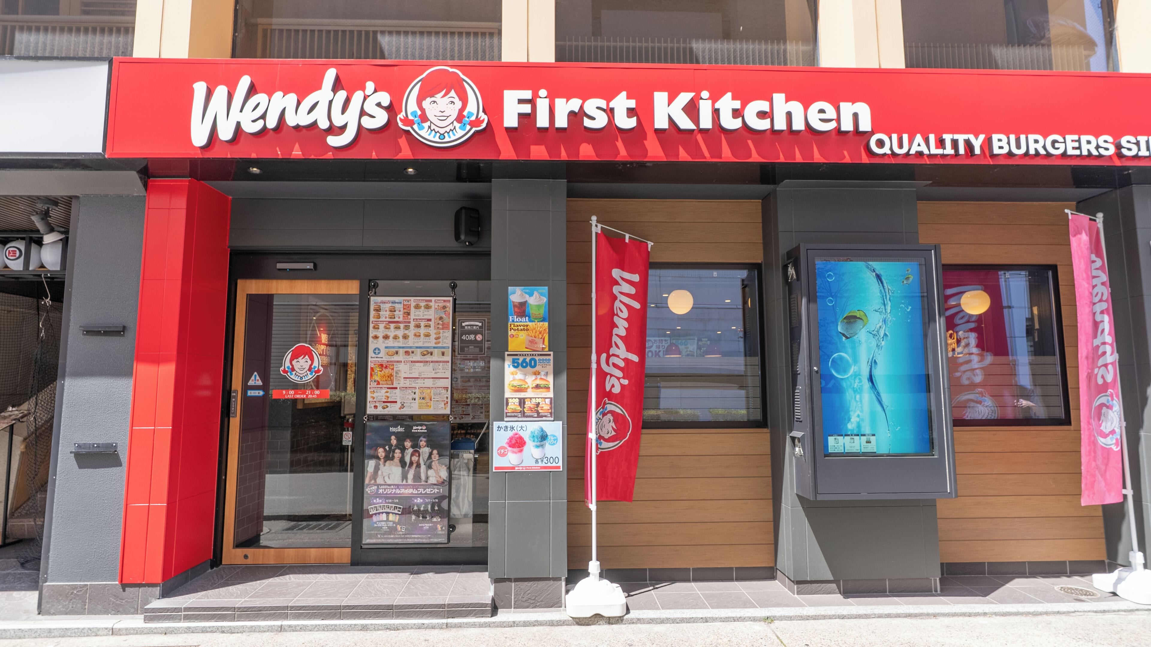 Un restaurante Wendy's First Kitchen con fachada roja y negra, un menú y un amplio ventanal que muestra el interior.