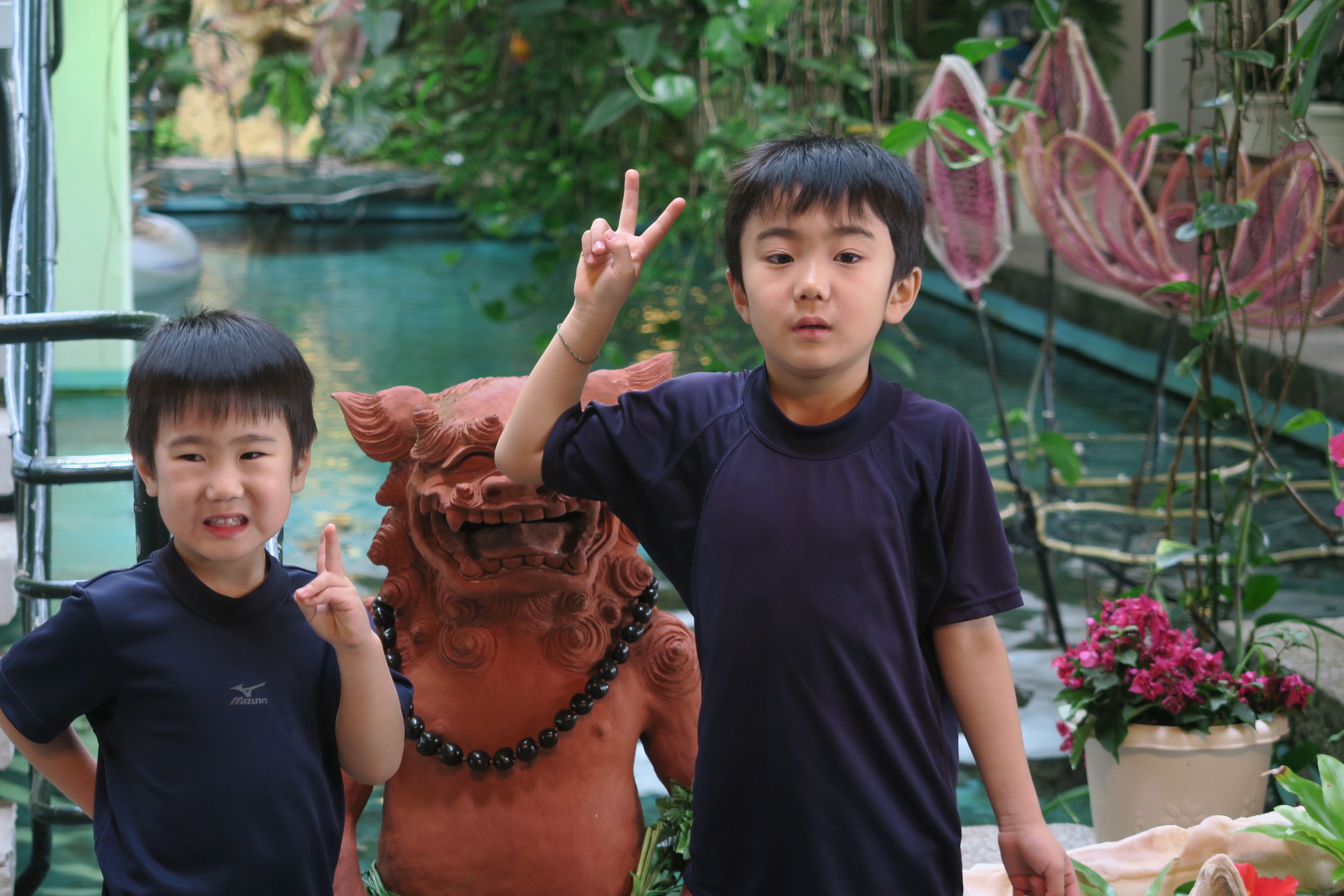 Deux personnes se tiennent à côté d’une statue en terre cuite dans un jardin, avec un bassin et des plantes en pot.