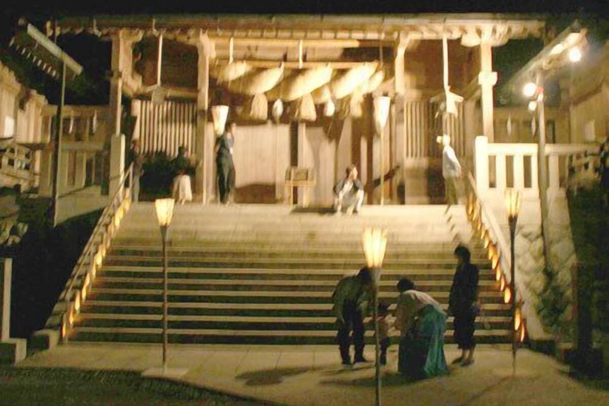 A building with a staircase leading to a covered entrance, a few people near the steps, and a street lamp in the foreground.