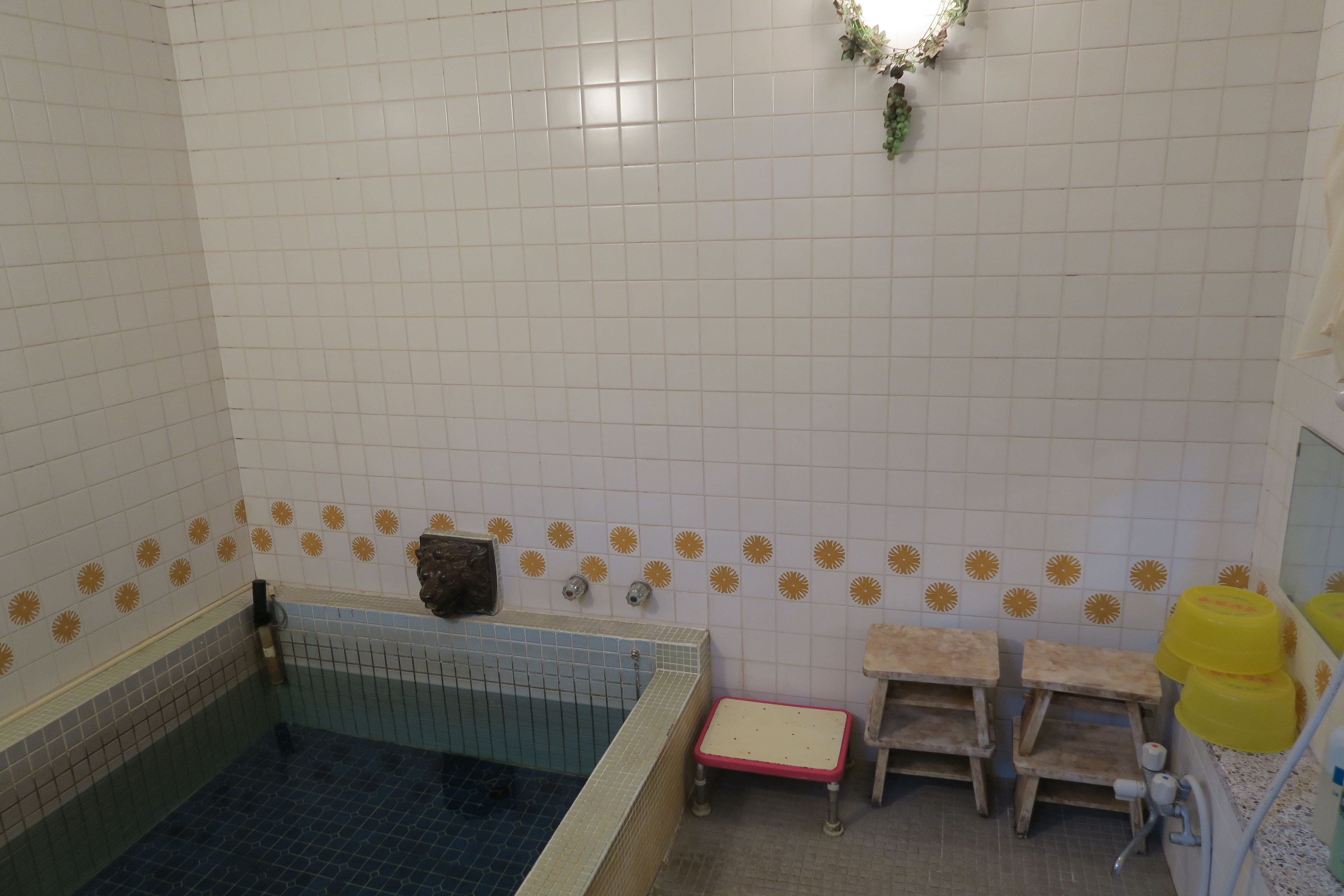 A bathroom with a bathtub, a small wooden stool, a yellow bucket, and a wall-mounted shelf.