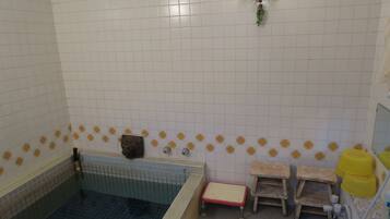 A bathroom with a bathtub, a small wooden stool, a yellow bucket, and a wall-mounted shelf.