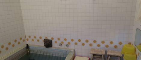A bathroom with a bathtub, a small wooden stool, a yellow bucket, and a wall-mounted shelf.
