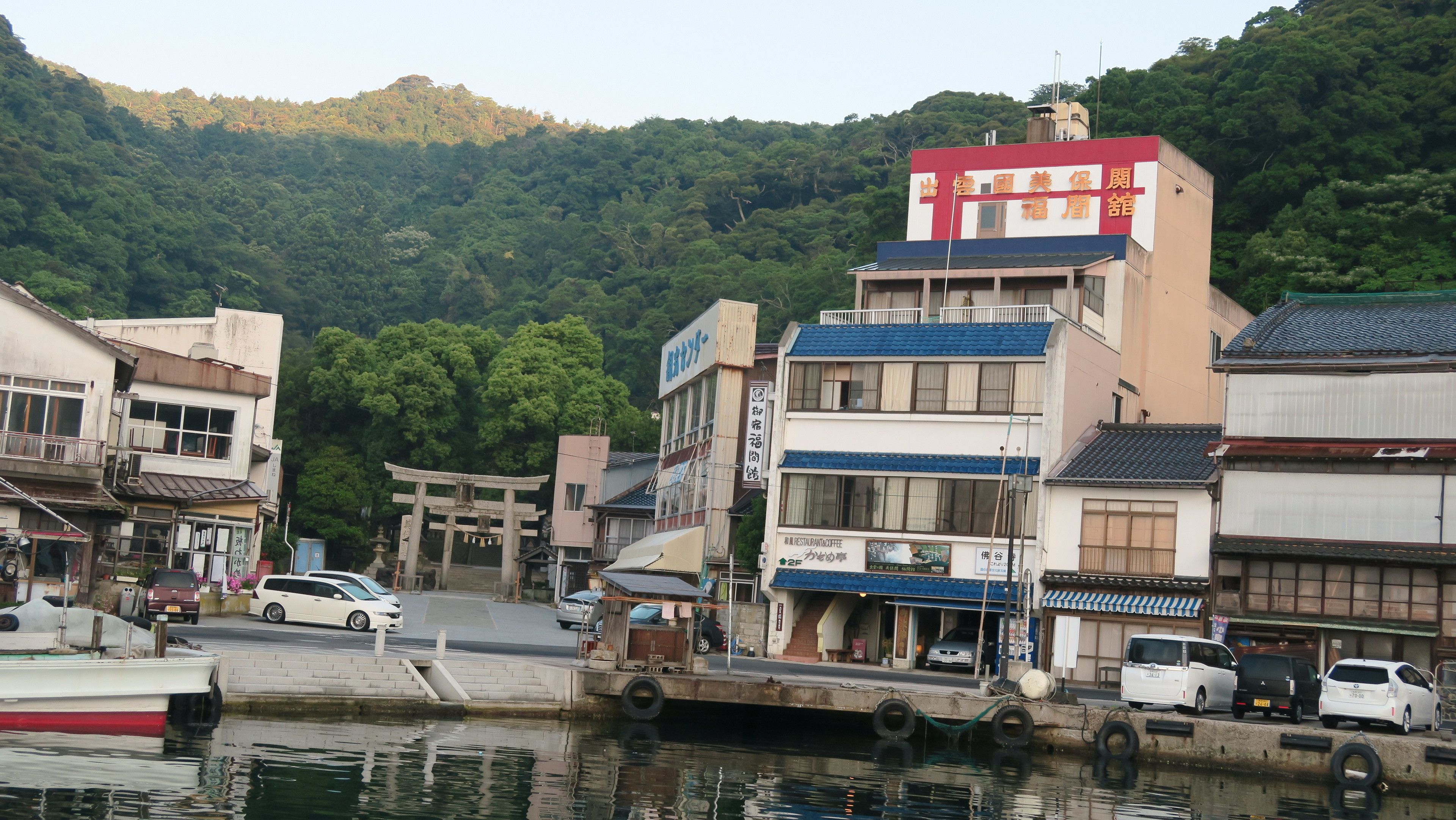 A traditional Japanese town with buildings, a torii gate, and a dock with boats.