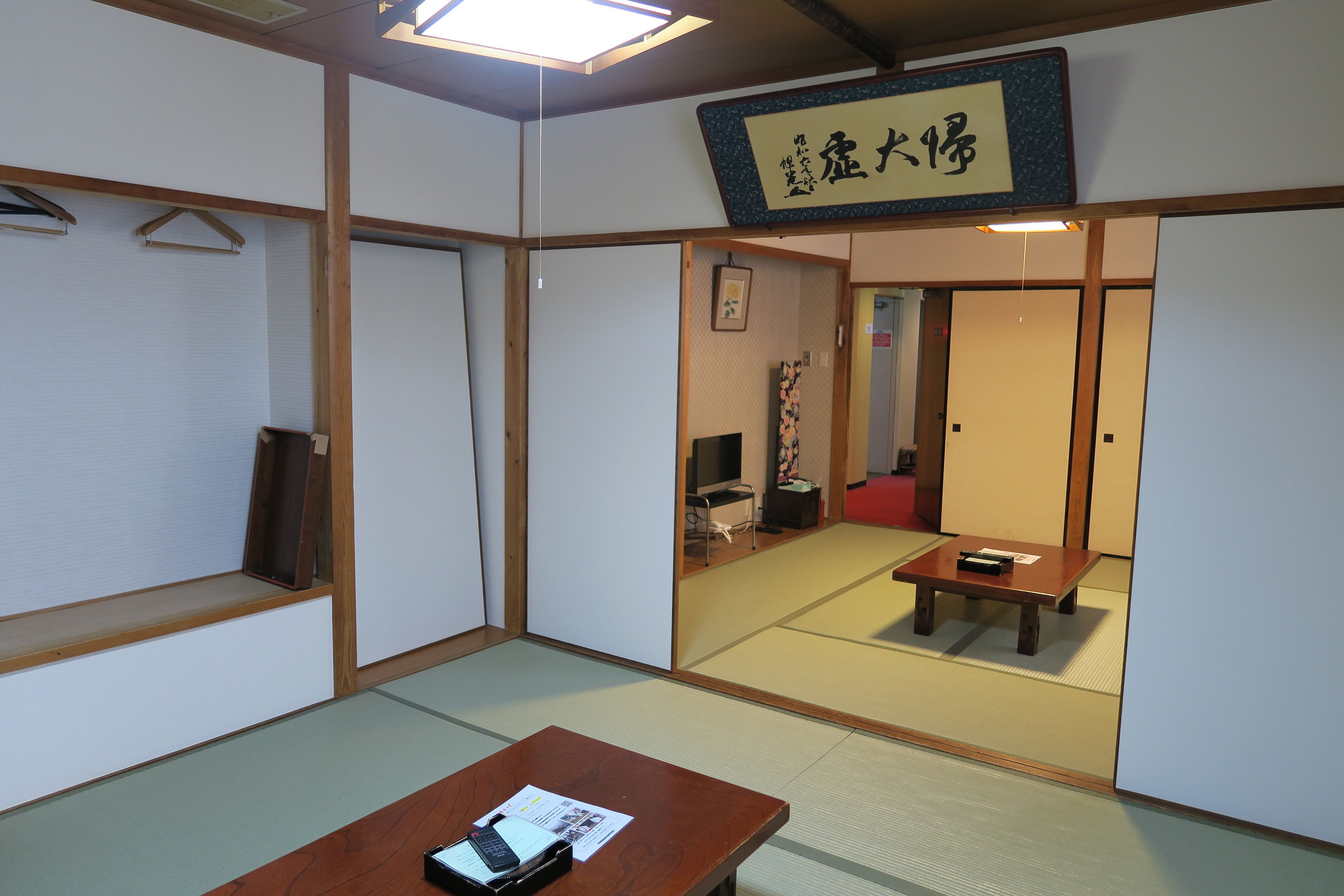 A traditional Japanese room with tatami flooring, a low wooden table, and a hanging sign with Japanese characters.