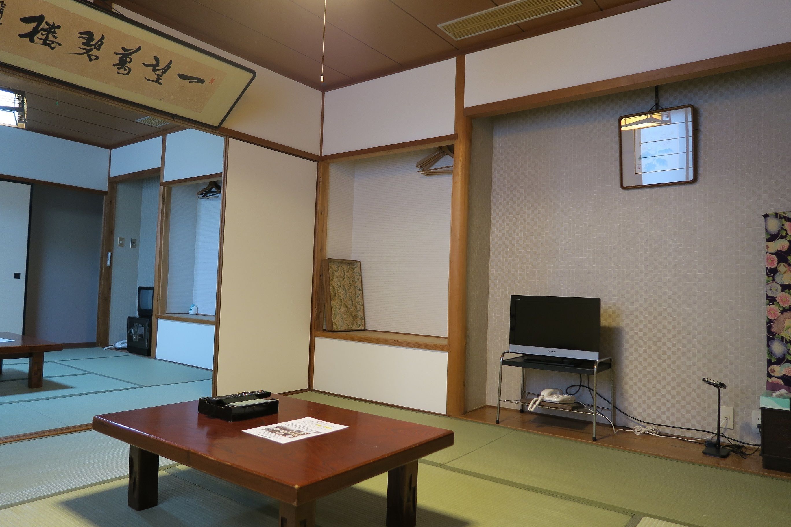 Une pièce de style japonais traditionnel, avec un sol recouvert de tatamis, une table en bois, un téléviseur et une petite étagère sur laquelle se trouvent un téléphone et un haut-parleur.