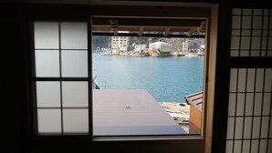 Vista a través de una ventana con un diseño de cuadrícula, sobre un cuerpo de agua con barcos y edificios a lo lejos.