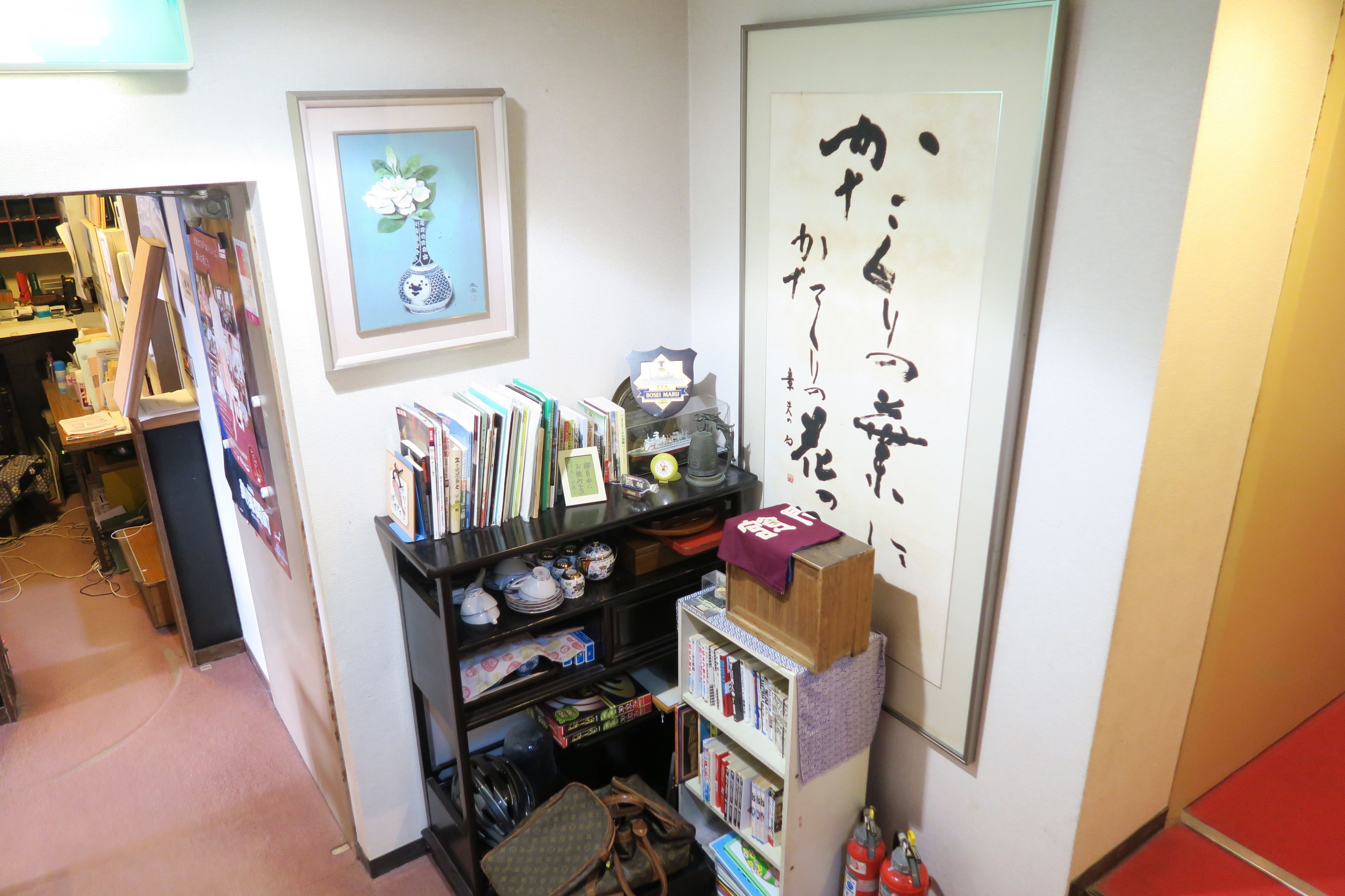 A room with a bookshelf, framed artwork, and a large calligraphy piece on the wall.