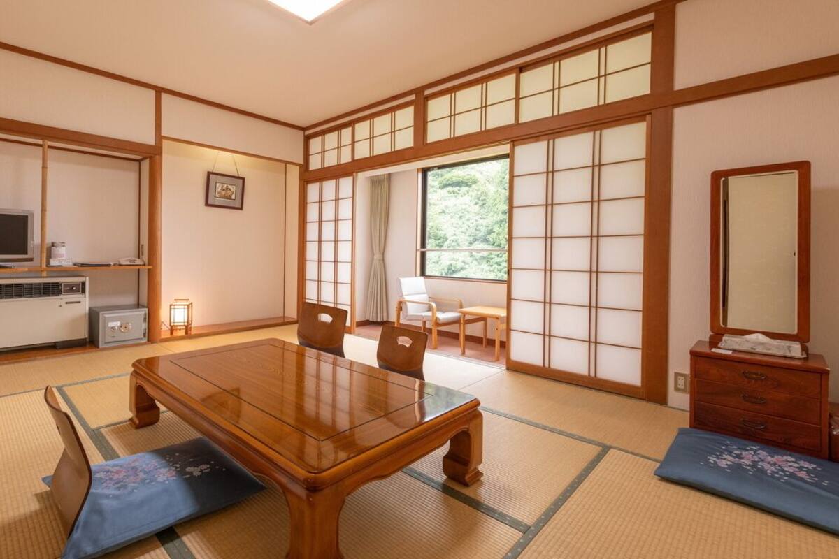 A traditional Japanese room with tatami flooring, a wooden table, chairs, a television, and sliding doors.