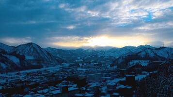 A town nestled between snow-covered mountains with a clear sky and the sun setting in the background.