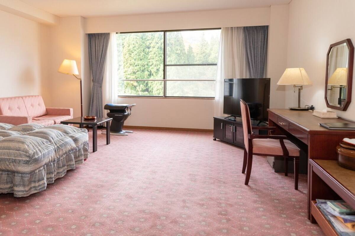 A hotel room with a bed, a desk, a chair, a television, and a window with curtains.