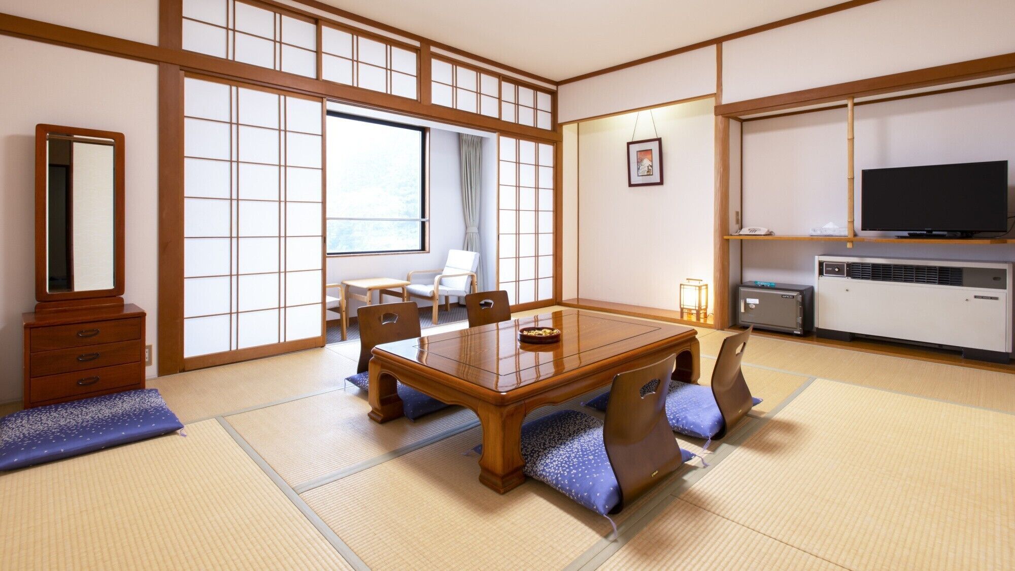 A traditional Japanese-style room with tatami flooring, a low table with cushions, a television, and a cabinet.