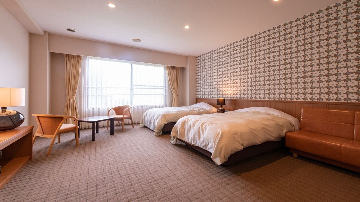 A hotel room with two beds, a sofa, a desk with a lamp, and a patterned wall.