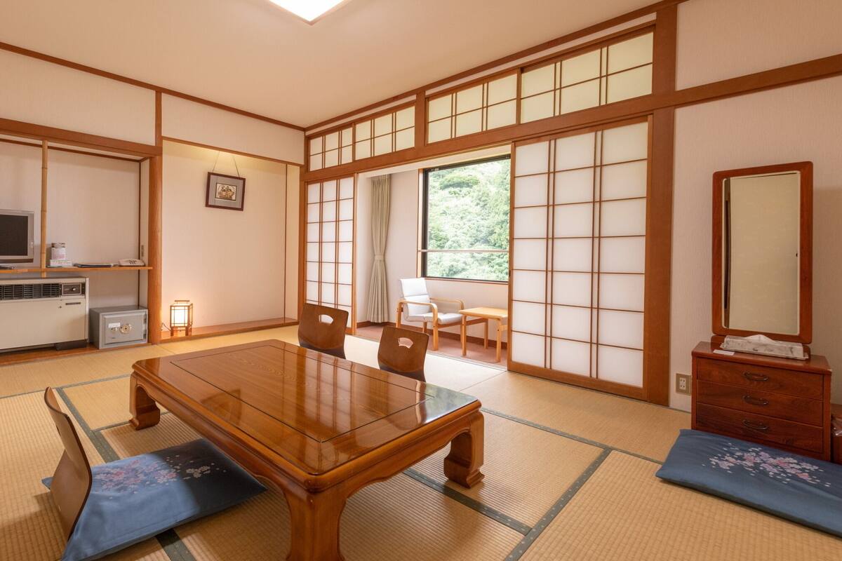 A traditional Japanese room with tatami flooring, a wooden table, a television, and a sliding door leading to a balcony.