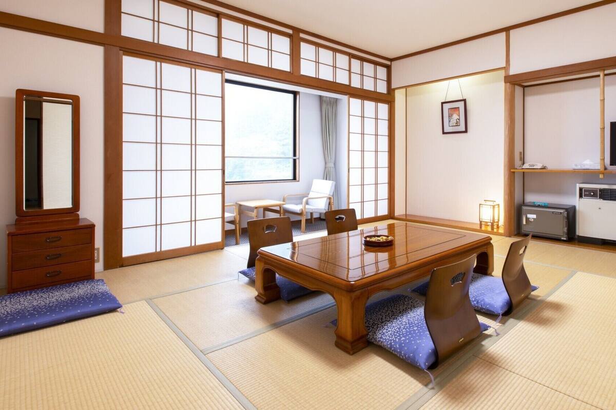 A traditional Japanese room with tatami flooring, a wooden dining table, a TV, and a cabinet.