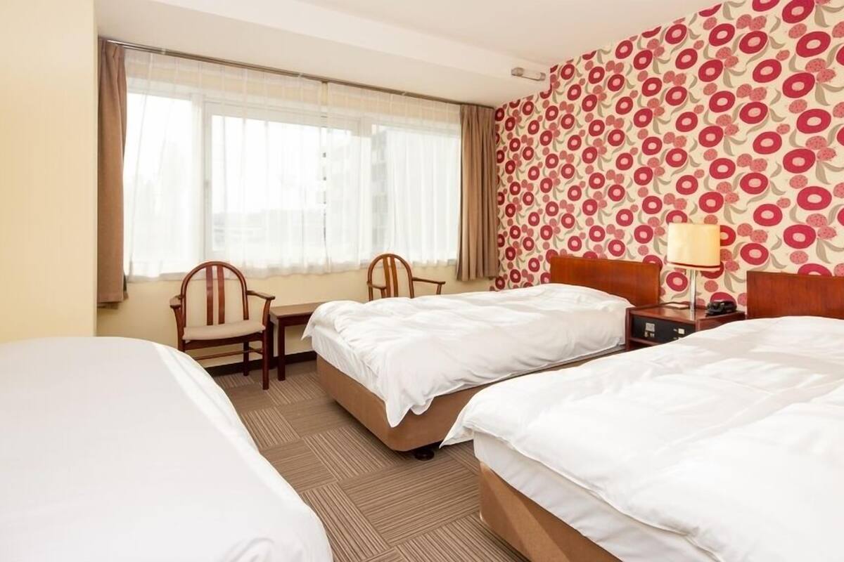 A hotel room with two beds, a desk, a chair, and a patterned wall.