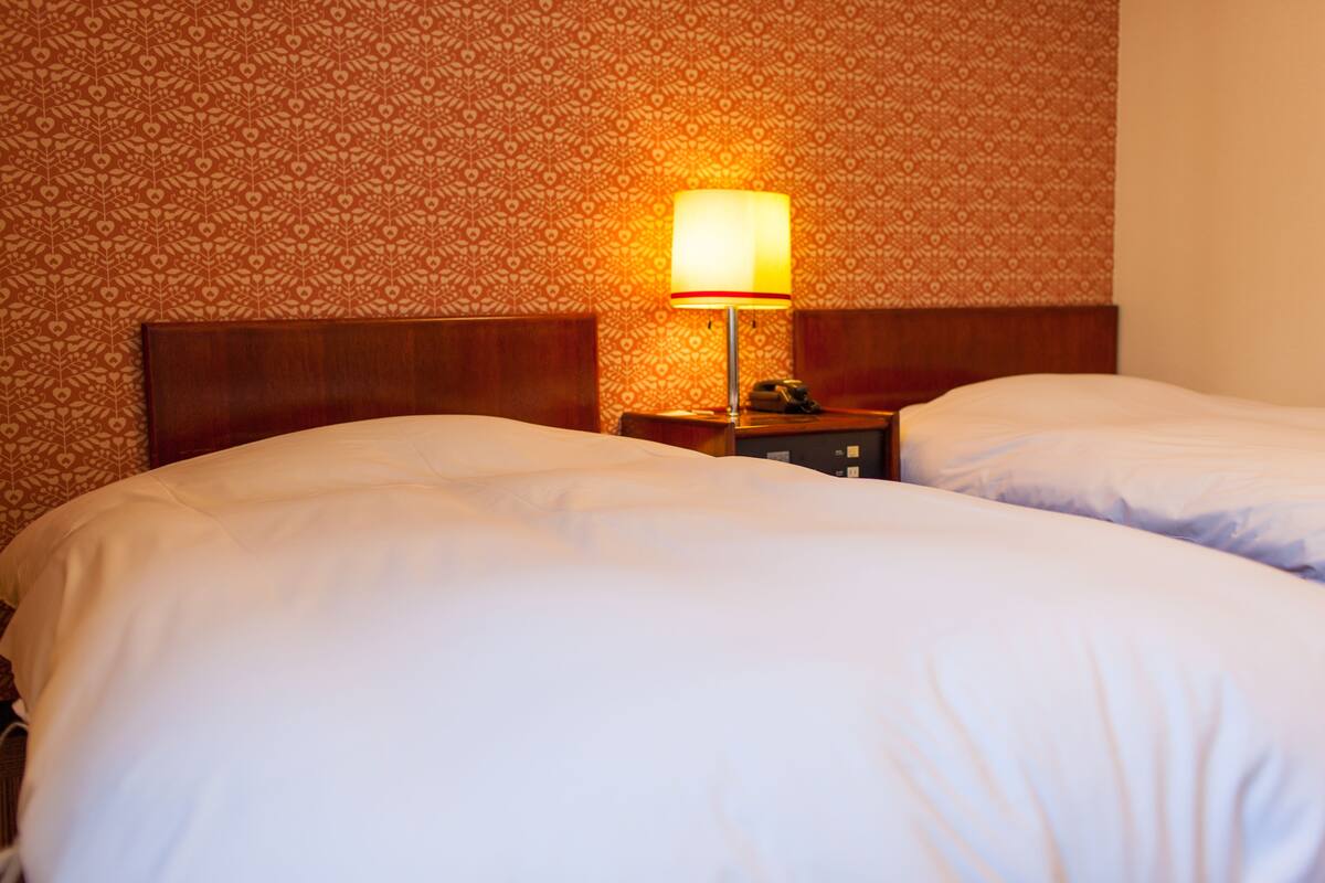 A hotel room with two beds, a patterned wallpaper, and a nightstand with a lamp.
