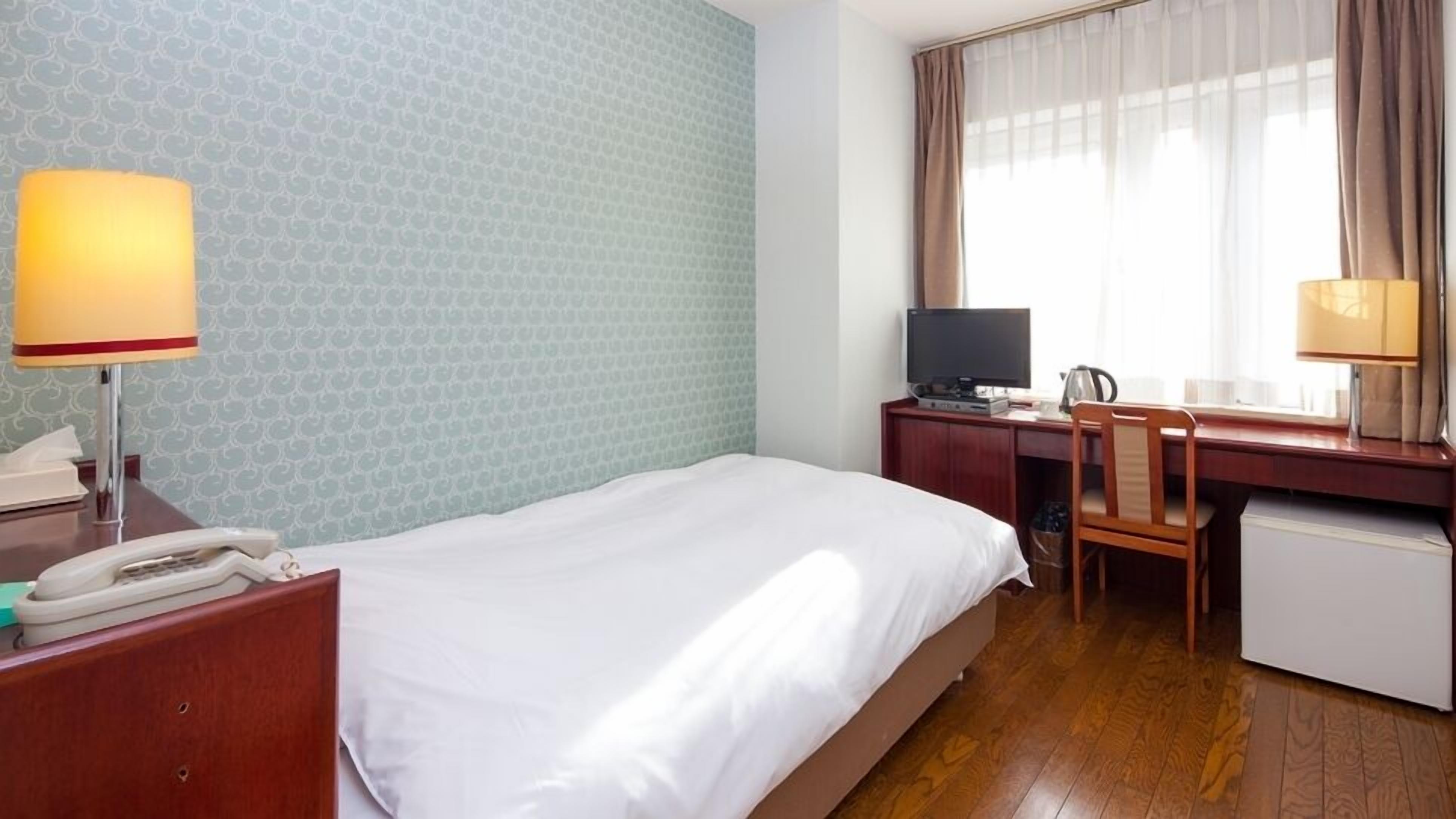 Una habitación de hotel con cama, escritorio, silla, televisor y teléfono.