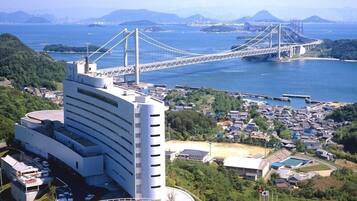 A modern building with a curved facade, located near a coastal area with a large bridge in the background.