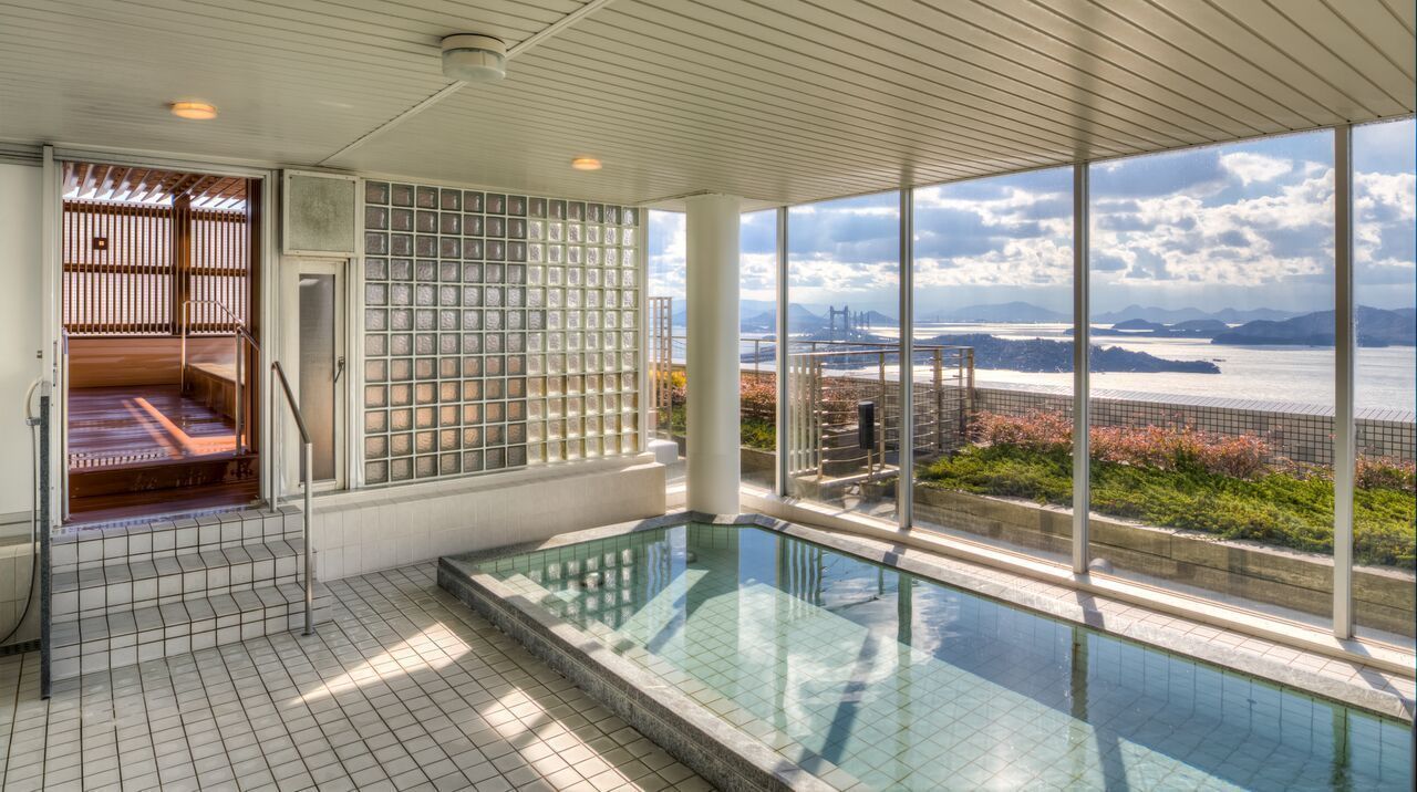 Una piscina interior moderna con cerramiento de vidrio, un área de sauna y vistas a un cuerpo de agua y montañas distantes.