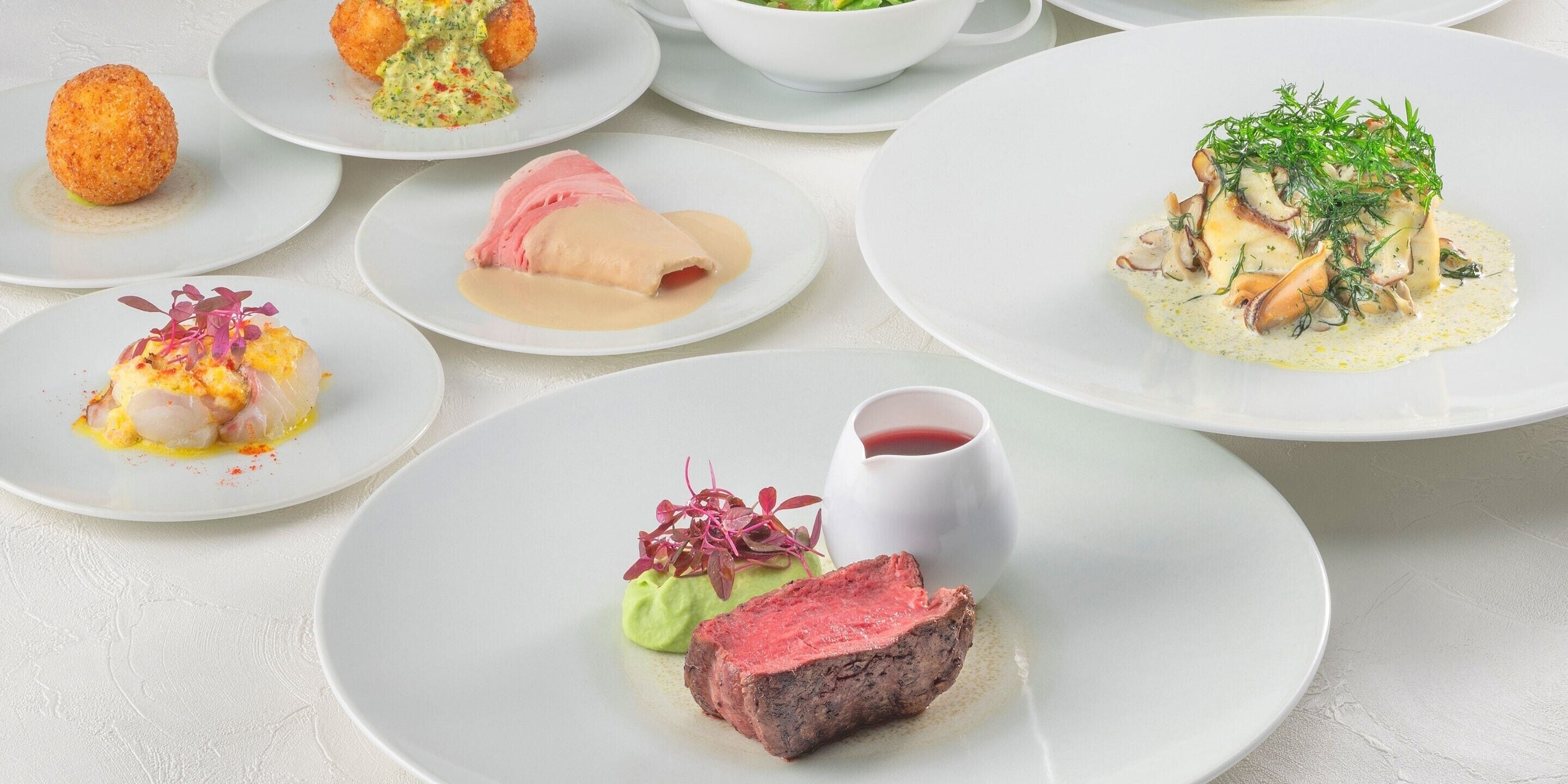 A variety of plated dishes, including seafood, meat, and vegetables, arranged on white plates.