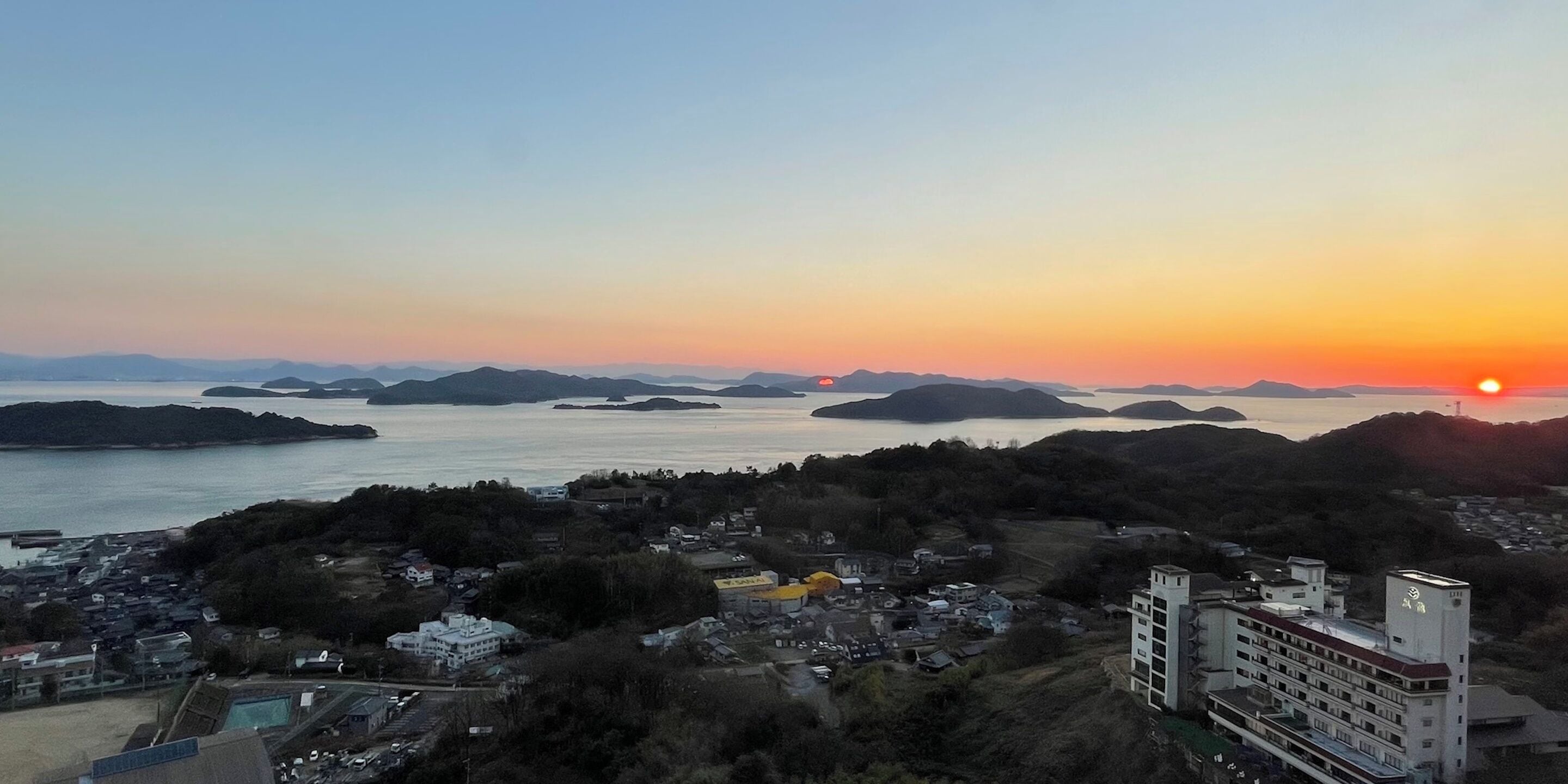 A coastal town at sunset with buildings and a body of water.
