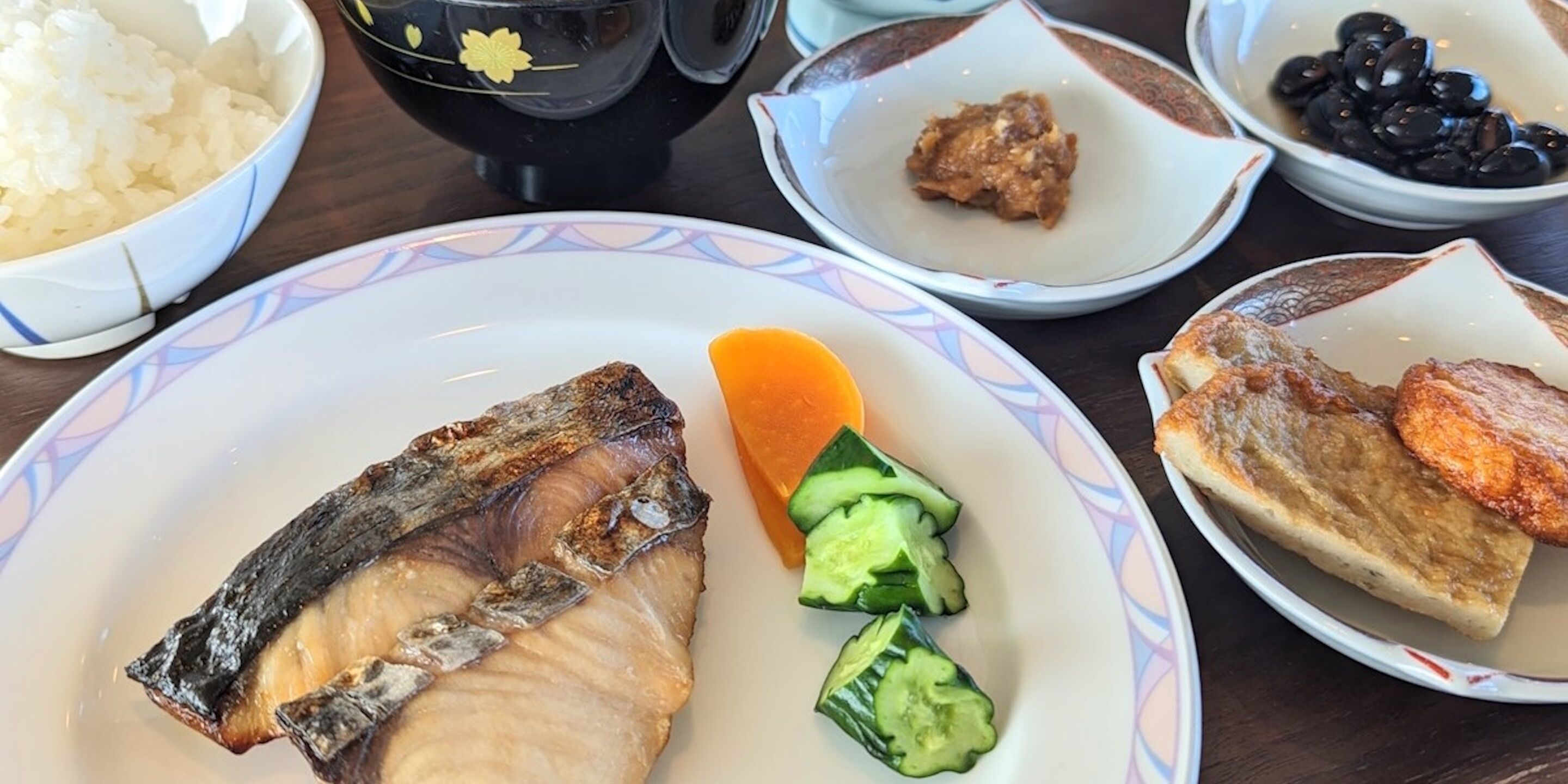 A table with various dishes including fish, cucumber slices, and a bowl of rice.