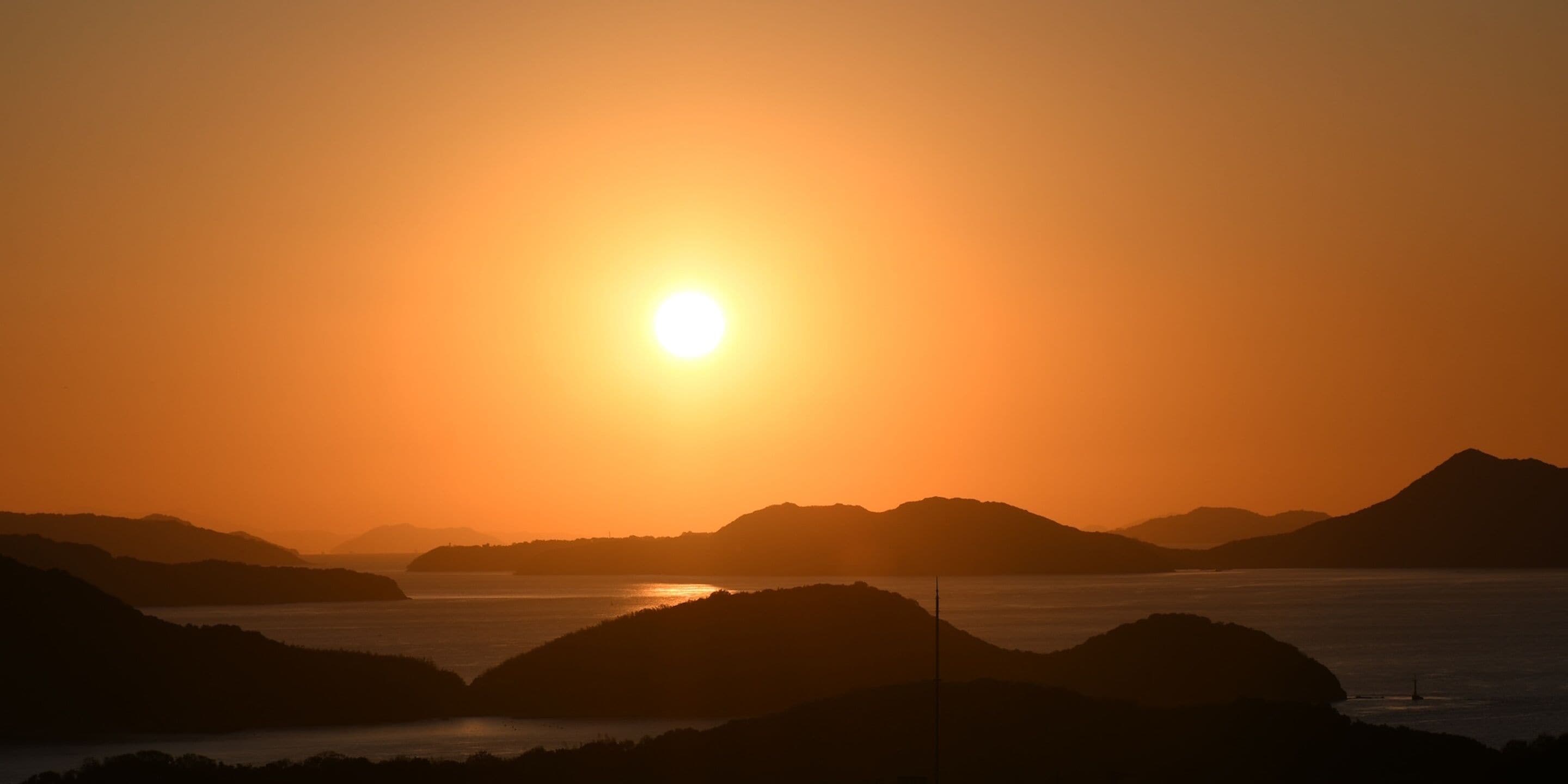 Un coucher de soleil sur un paysage montagneux, avec une étendue d'eau au premier plan.