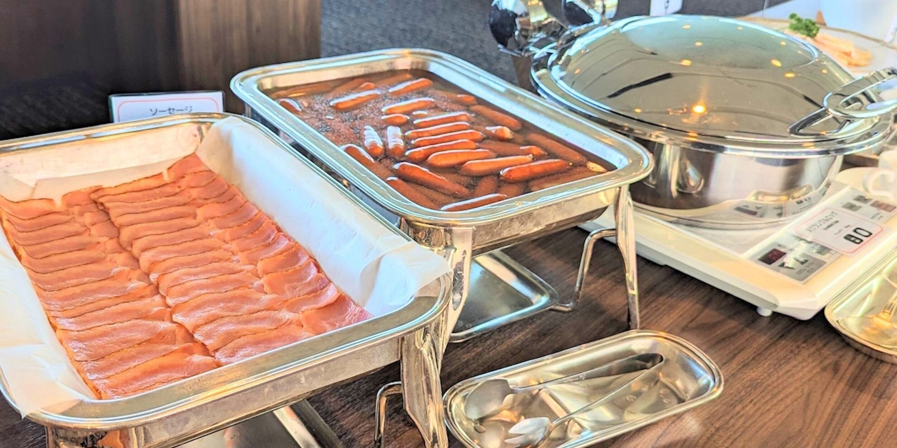 A buffet setup with various food items including sliced meats and hot dogs.